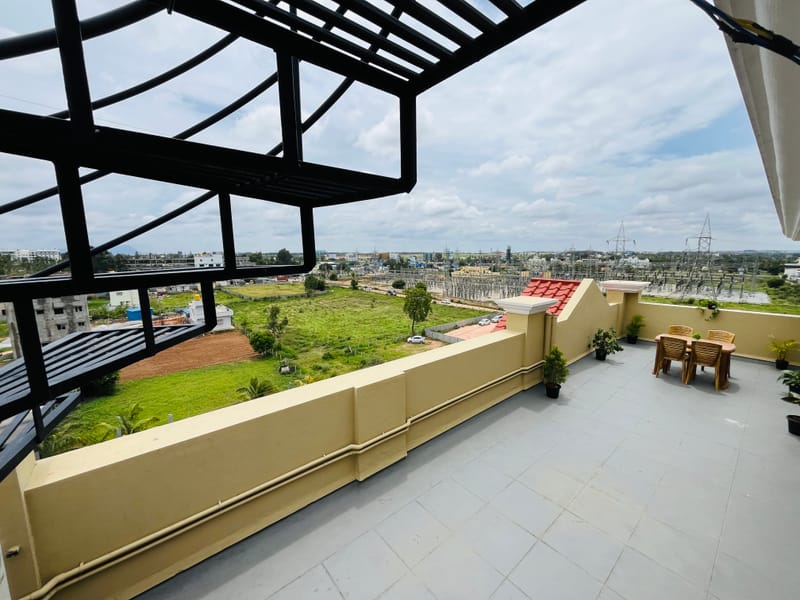 Pergola shaded rooftop terrace at Value Inn, Bangalore Airport with garden chairs, potted plants, and wide views of the surrounding greenery