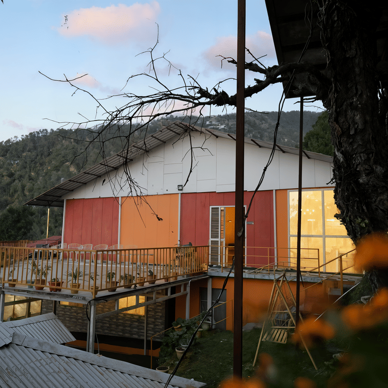 Terracotta-roofed cottage building of Nazaara Nature Retreat set against layered mountain ridges under a dusky evening sky