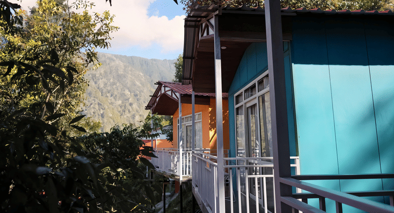 Balcony walkway lined with teal and orange cottage doors at Nazaara Nature Retreat, mountain views in daylight
