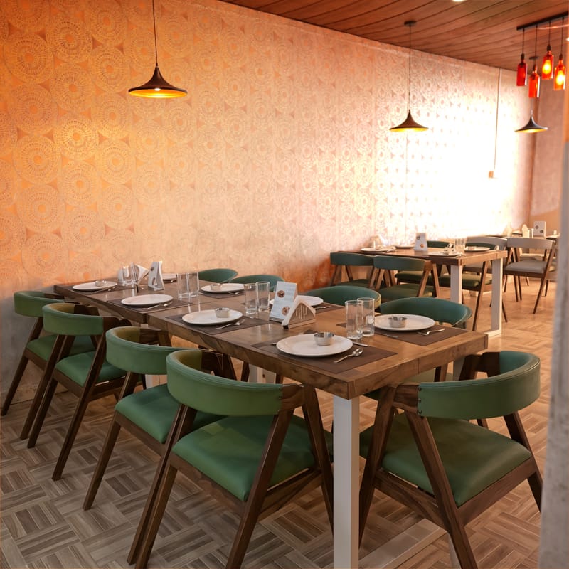Fine Dine restaurant at Nazaara Nature Retreat with green upholstered chairs set against richly patterned wallpaper