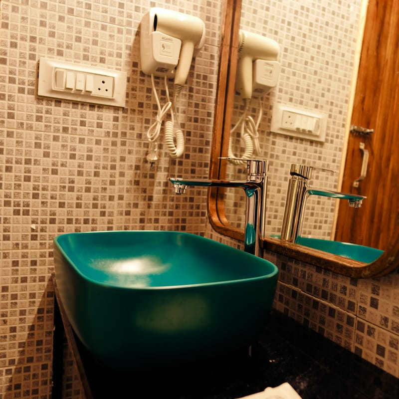 Close-up of the teal vessel sink and rustic wood-framed mirror in a Luxe Cottage bathroom at Nazaara Nature Retreat