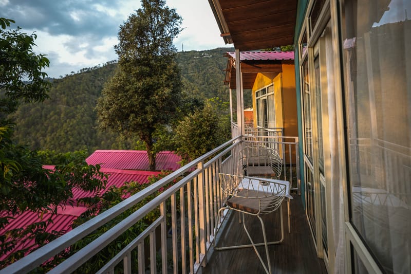 Premium Cottage private balcony at Nazaara Nature Retreat overlooking the pine-forested hillside beneath an open sky