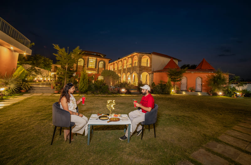 A couple seated for dinner on the lawn at Nazaara Hills Retreat, Udaipur.