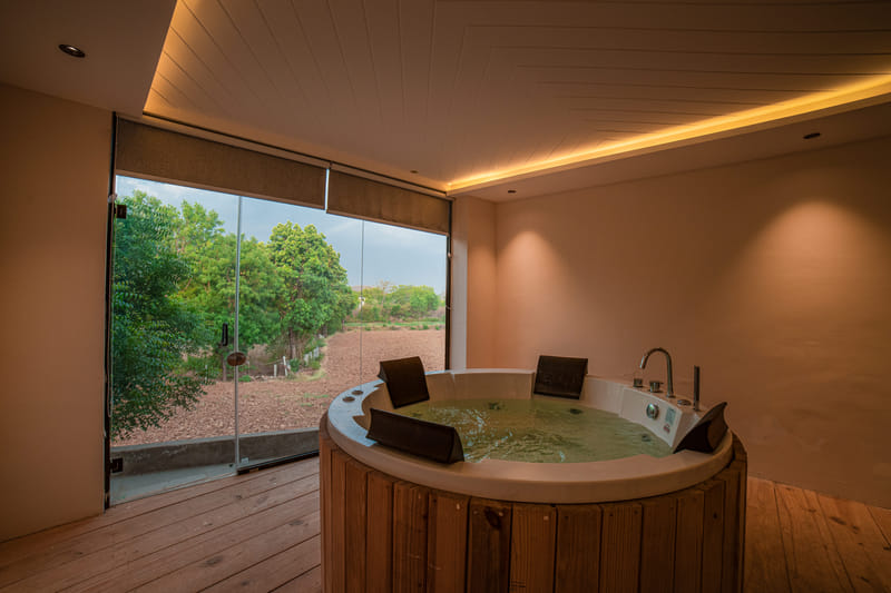 A wooden-framed Jacuzzi tub at Nazaara Hills Retreat, Udaipur, overlooking farmland at dusk.