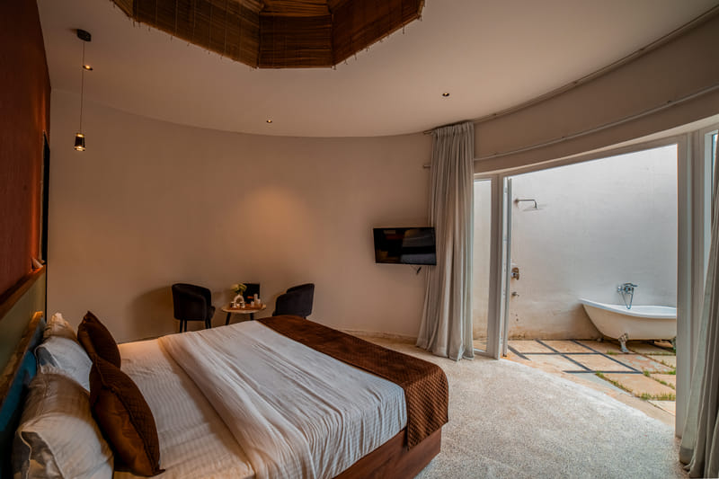 The Luxurious Cabana Cottage bedroom at Nazaara Hills Retreat, Udaipur, with a view of the outdoor tub.