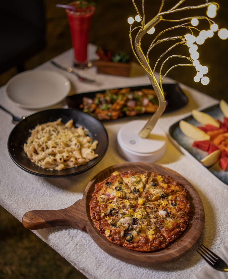 A table spread of pizza and pasta at Nazaara Fine Dine, Nazaara Hills Retreat, Udaipur.