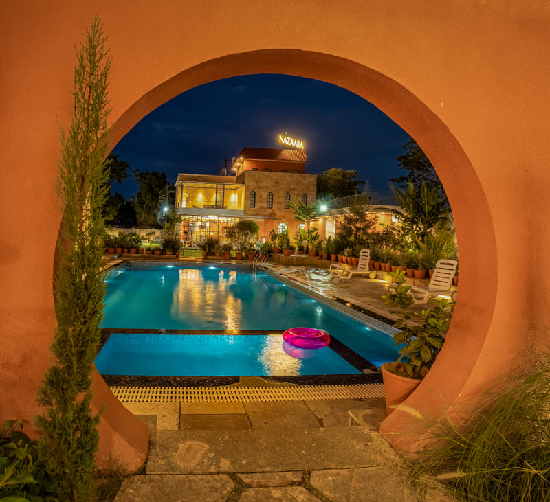 The swimming pool at Nazaara Hills Retreat, Udaipur, seen through an archway, lit at night.