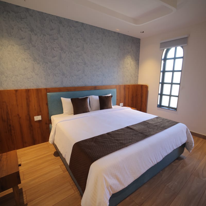 The Premium Plunge Pool Room bed positioned beside a window at Nazaara Hills Retreat, Udaipur.