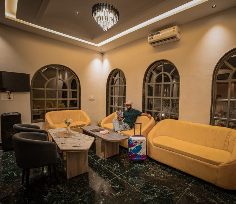 Reception lounge seating at Nazaara Hills Retreat, Udaipur, with a television and arched windows.