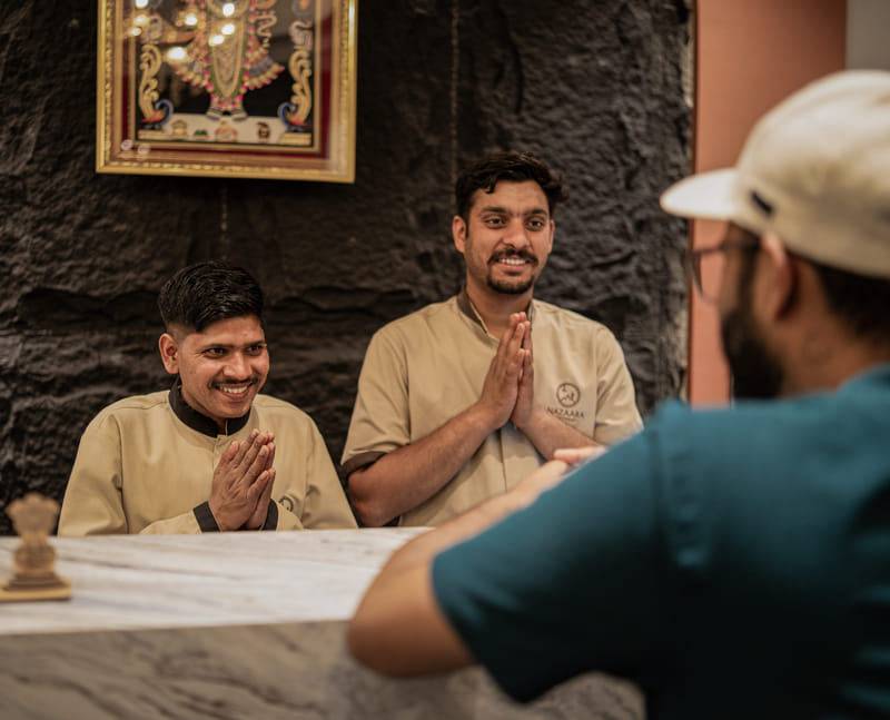 A staff member greeting guests with a namaste at Nazaara Hills Retreat, Udaipur.