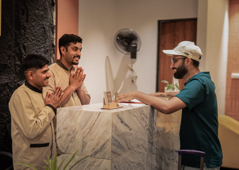 Staff greeting an arriving guest with luggage at the reception of Nazaara Hills Retreat, Udaipur.