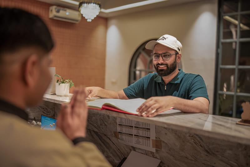 A staff member showing a rate card to a guest at the reception desk of Nazaara Hills Retreat, Udaipur.