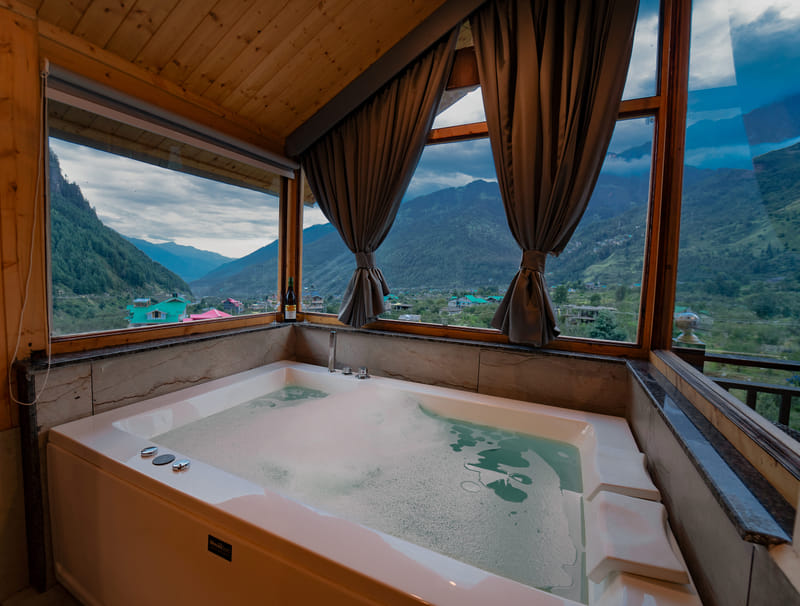 Jacuzzi tub filled with bubbles in the Nazaara Luxe Interconnected room, mountain view through the window