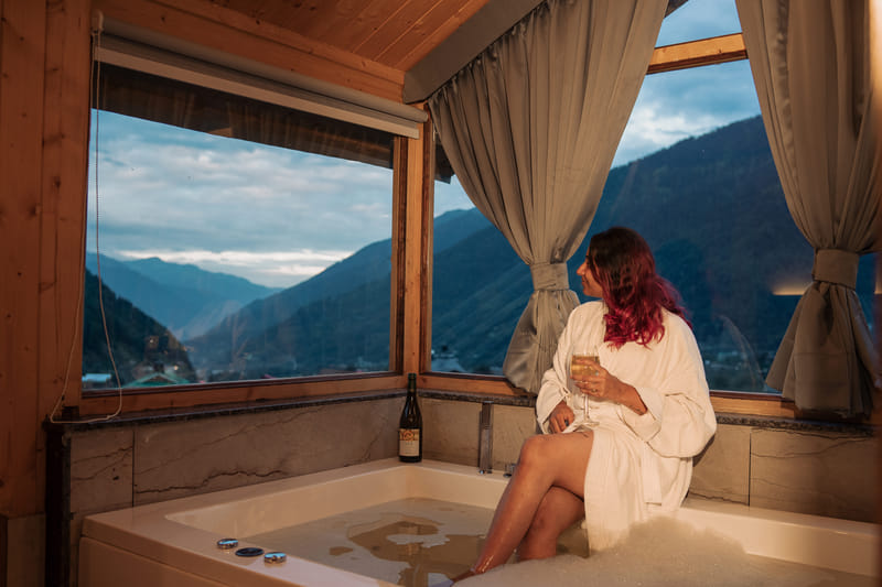 A guest in a bathrobe beside the Jacuzzi tub in the Nazaara Luxe Interconnected room
