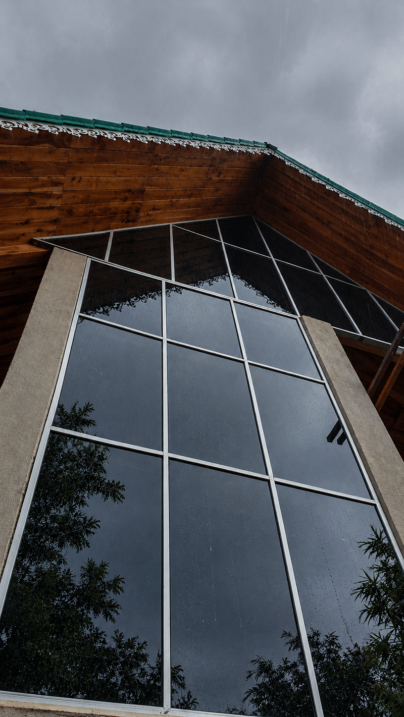 A tall glass facade in dark frames rising beneath a gabled timber roof at The Garud Forest, Tadoba