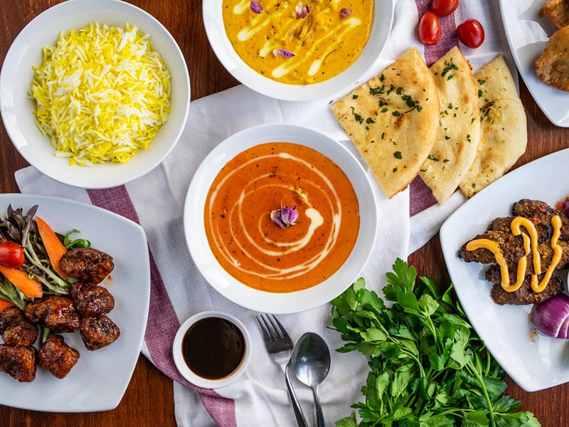 A spread of Indian dishes with saffron rice, curries, and breads laid out on white plates at The Garud Forest, Tadoba