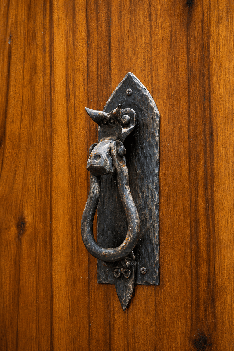 A wrought-iron ring handle on a warm, grained teak door at The Garud Forest, Tadoba