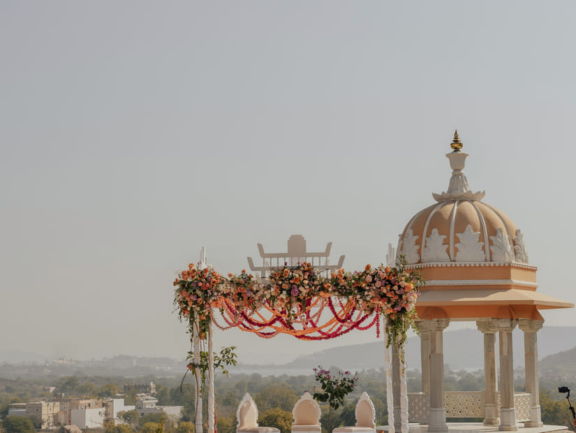 A wedding set up featuring a decorated canopy and a small architectural structural surrounded by plans and flowers.