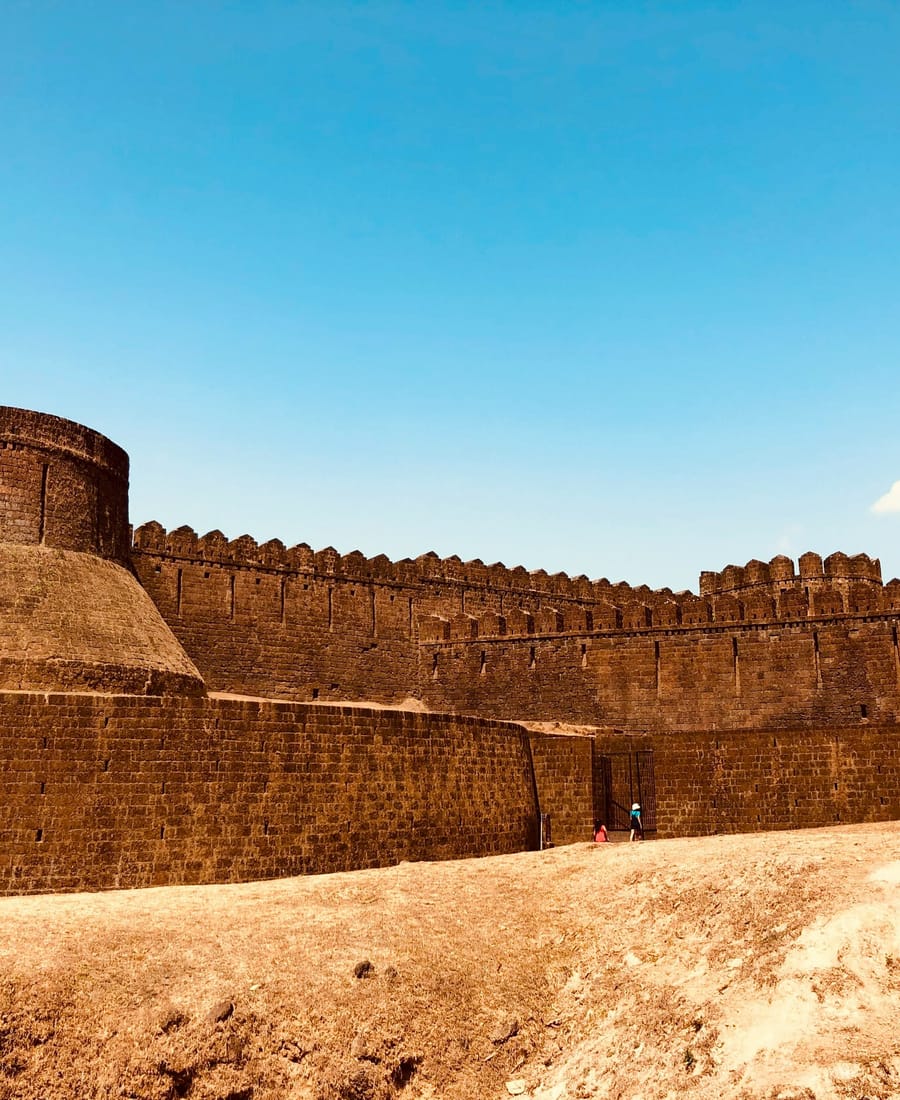 Devanahalli Fort near Bangalore Airport, with a round stone bastion and a long crenellated rampart wall rising over bare ground under a clear blue sky