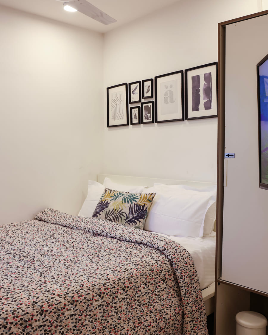 Bedroom of Room 502 at Wabi-Sabi, Juhu, closer view of the leaf-print cushion and headboard beside a wardrobe with an arrow decal and a TV showing tea fields.