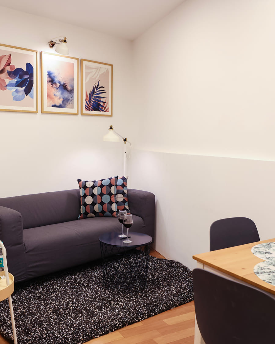 The Room 501 living room at Wabi-Sabi, Juhu with a grey sofa, patterned cushion, round coffee table, dining table with 2 chairs, and a fruit tray.