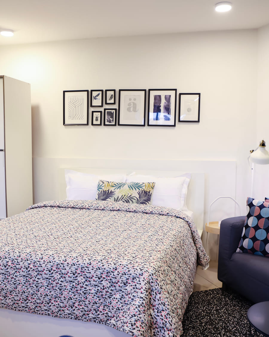 Bedroom at Wabi-Sabi, Juhu, with a patterned bedspread, a white wardrobe, a gallery wall of framed prints, and a navy sofa with printed cushions.
