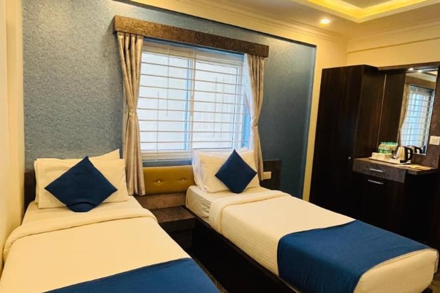 2 single beds with blue cushions and runners beside a bright window in the Standard AC Twin Room at Value Inn, Bangalore Airport