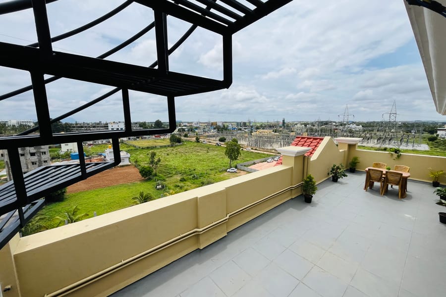 Pergola shaded rooftop terrace at Value Inn, Bangalore Airport with garden chairs, potted plants, and wide views of the surrounding greenery