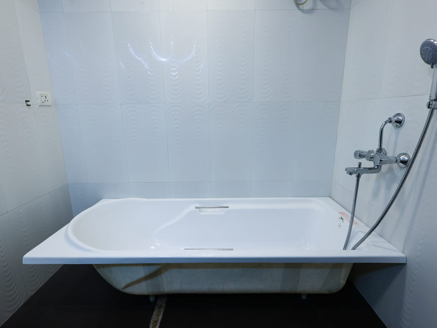 The Room 401 bathroom at Wabi-Sabi, Juhu with a white bathtub against tiled walls and a wall-mounted handheld shower with chrome fittings.