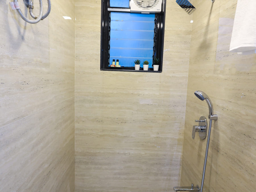 Bathroom of Rooms 402 and 5001 at Wabi-Sabi, Juhu, showing the shower stall with an overhead rain shower, handheld sprayer, and a small window with plants.