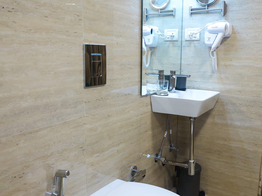 Bathroom of Rooms 402 and 5001 at Wabi-Sabi, Juhu, showing a wall-hung toilet with a handheld bidet spray beside the travertine-tiled sink area.