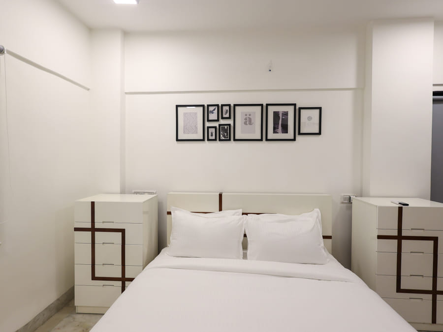 Bedroom of Room 401 at Wabi-Sabi, Juhu, viewed head-on with matching dressers flanking the bed and a centred gallery wall of framed art.