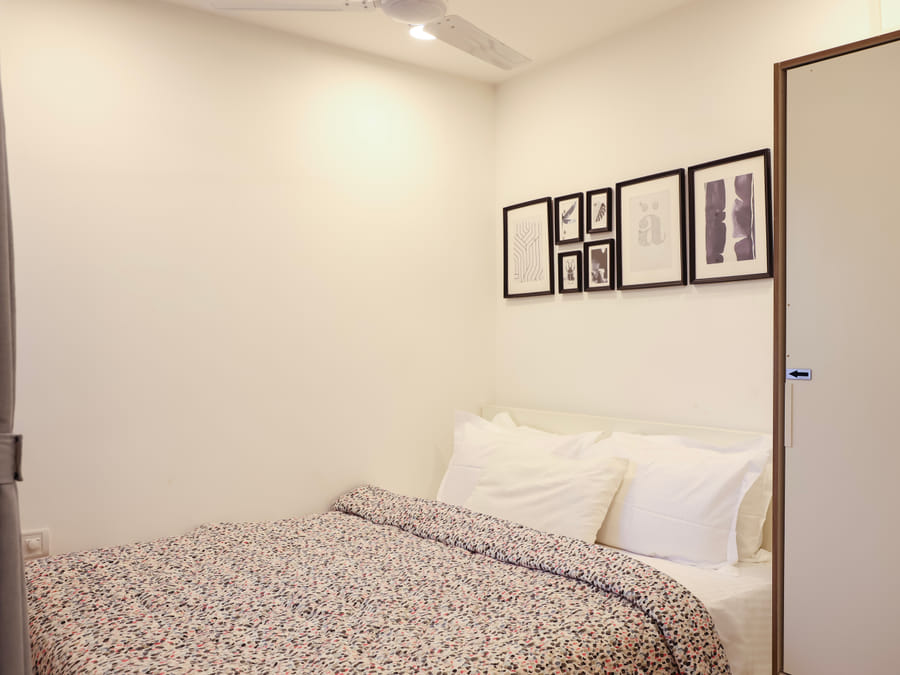 Bedroom of Room 502 at Wabi-Sabi, Juhu, with a speckled printed duvet, a tied-back grey curtain, a gallery wall of framed art, and a closed white wardrobe.