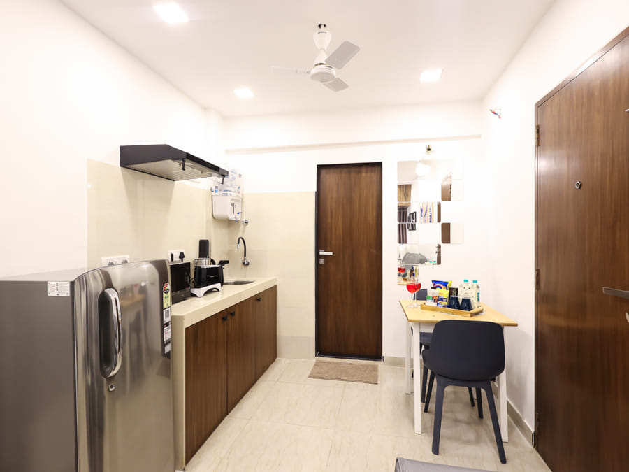 Entryway passage at Wabi-Sabi, Juhu, with a kitchenette on one side and a small dining table with 1 chair near the front door on the other.