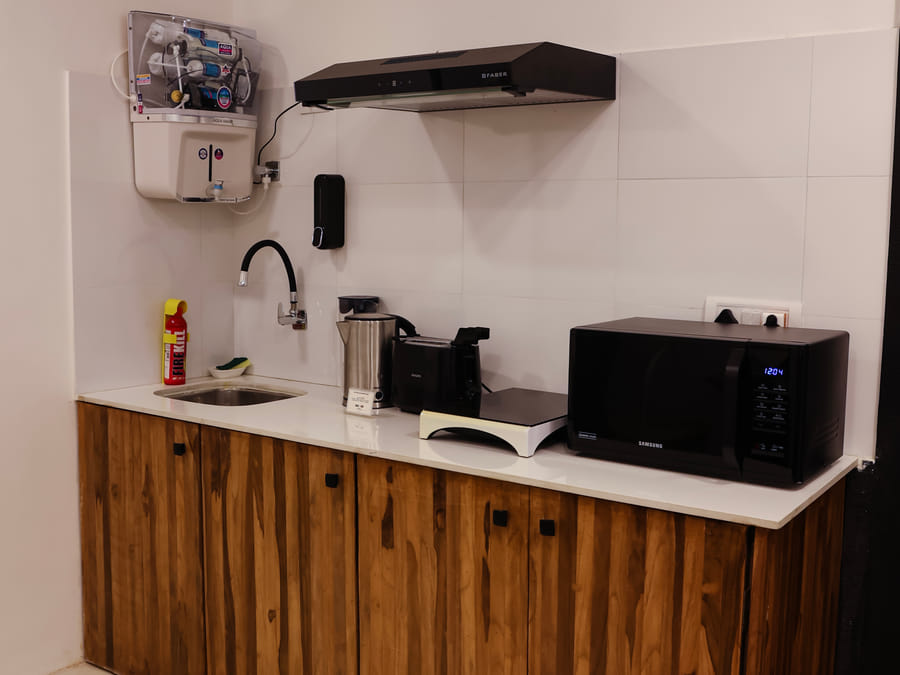 Kitchen in Room 501 at Wabi-Sabi, Juhu, with wooden cabinets, marble flooring, a wall clock, sink, exhaust hood, toaster, kettle, and microwave.