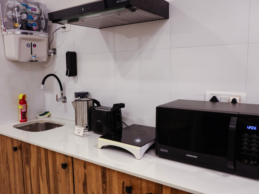 Kitchen counter in Room 501 at Wabi-Sabi, Juhu, with a sink, exhaust hood, induction cooktop, toaster, kettle, microwave, and a wall-mounted water purifier.
