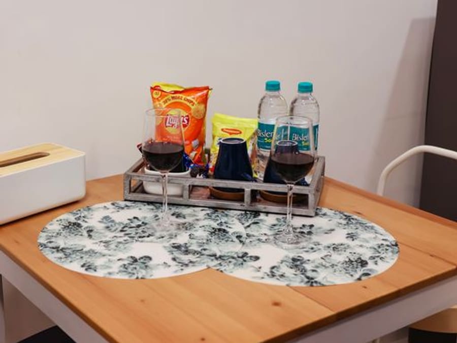 Dining table at Wabi-Sabi, Juhu, with 2 wine glasses, a tray of bottled water, a bag of chips, and a tissue box on a floral table runner.