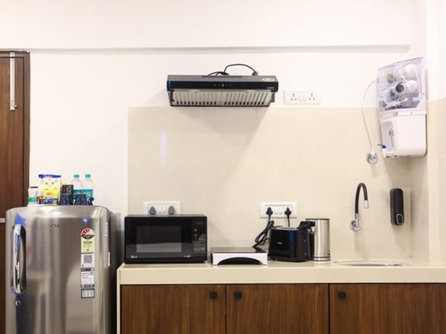 Kitchenette at Wabi-Sabi, Juhu, with a single-door fridge, microwave, toaster, kettle, exhaust hood, sink, and a wall-mounted water purifier.