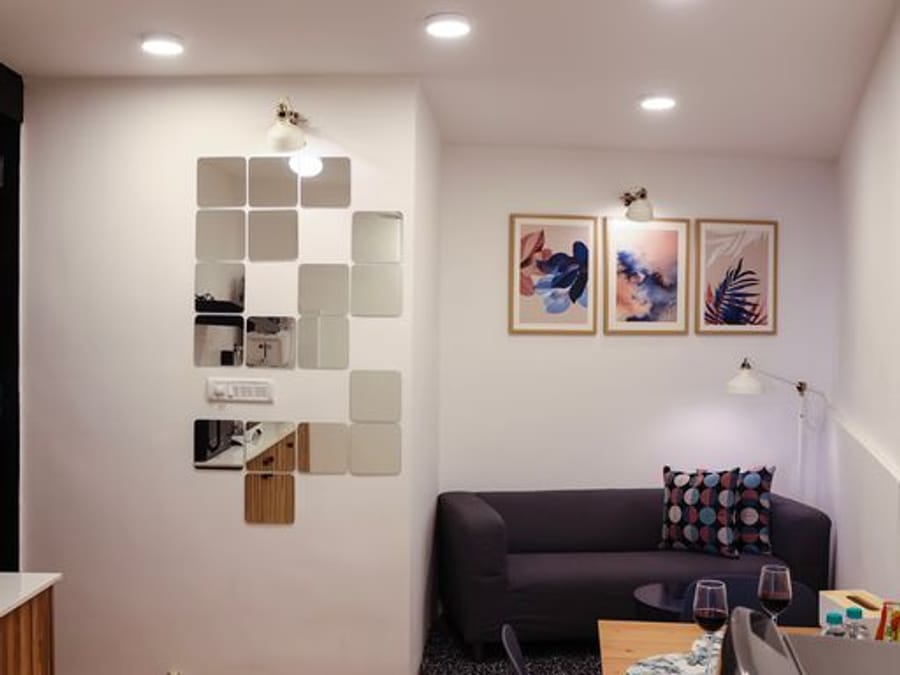Living area at Wabi-Sabi, Juhu, with a mosaic tile art wall, a dark grey sofa, framed floral prints, and a dining table set with wine glasses.