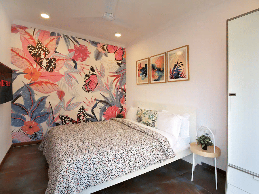 Bedroom at Wabi-Sabi, Juhu, with a floral butterfly mural wall, a matching printed duvet, three framed prints, and a white wardrobe beside the bed.