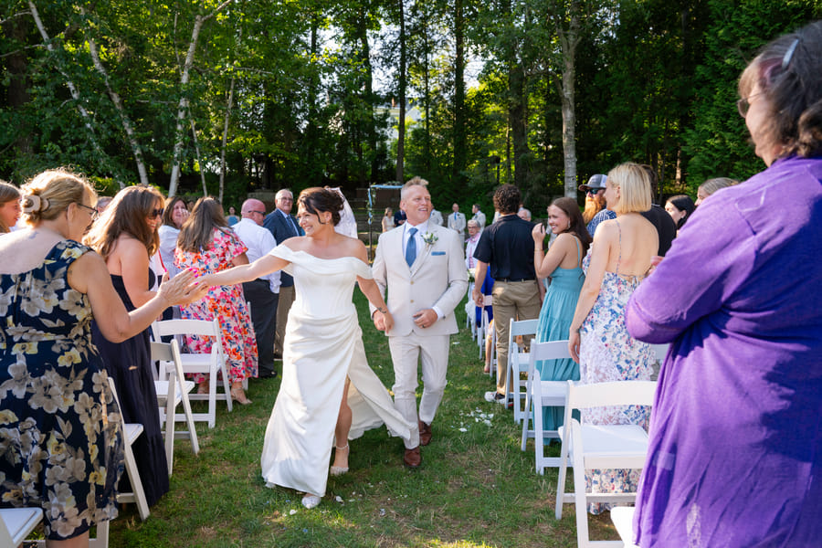 The newlyweds walking back down the garden aisle as guests applaud at Hartstone Inn