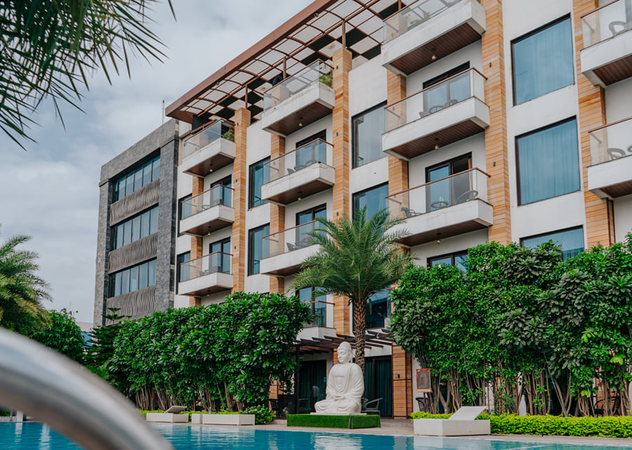 Multi-storey hotel building with balconies above palm trees and trimmed hedges