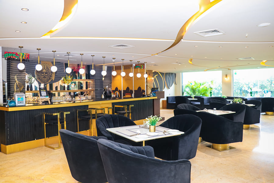 Zeus restaurant with black velvet armchairs, white tables and a gold-trimmed bar under globe lights