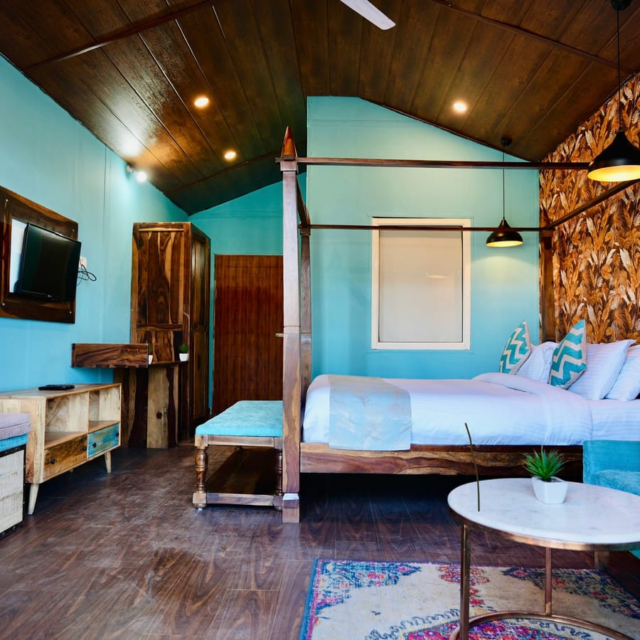 Four-poster bed with white linens in the Premium Cottage at Nazaara Nature Retreat, beside botanical-print wallpaper.