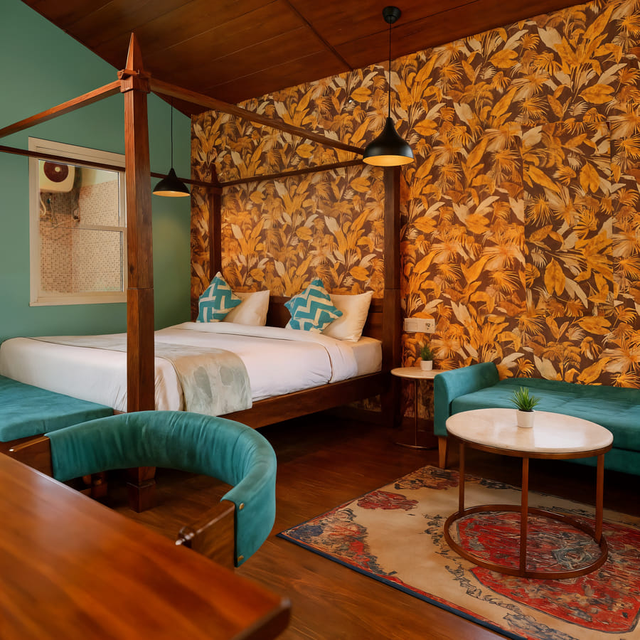 Four-poster bed and teal lounge corner in the Premium Cottage at Nazaara Nature Retreat, lit by a window in Dalhousie.