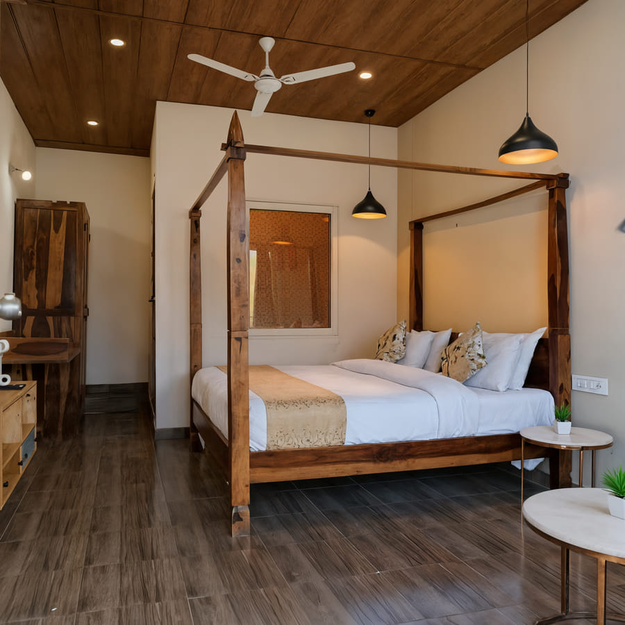 A king-size bed with a warm wooden headboard and soft linens in the Superior Room at Nazaara Nature Retreat, Dalhousie.