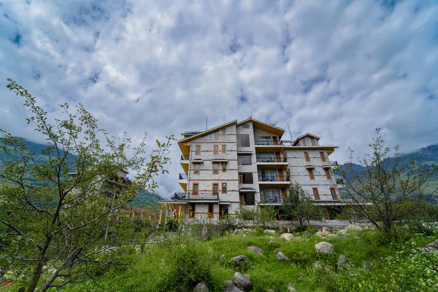 Nazaara Luxe Retreat's building seen across rows of apple trees, mountain slopes rising behind the orchard.