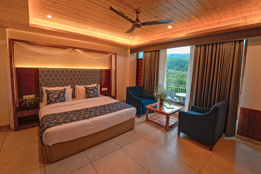 Bed and armchairs facing a forest view in the Luxurious Room at Nazaara Luxe Retreat, Manali
