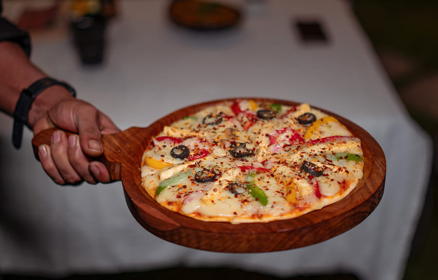 A pizza served on a wooden board at Restro & Café, Nazaara Luxe Retreat, Manali.
