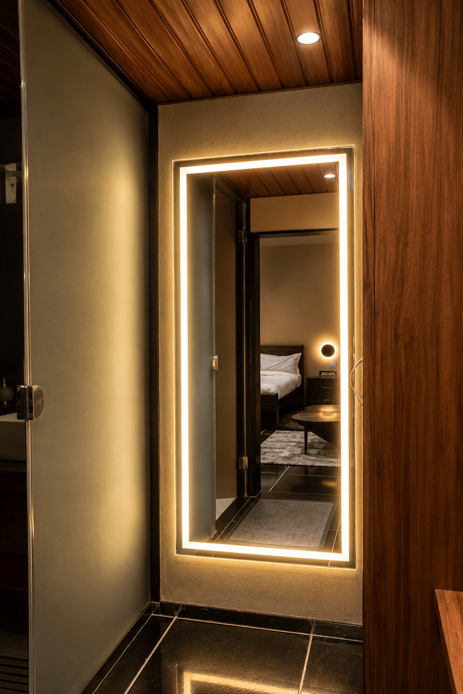 A bathroom entry lit by a backlit full-length mirror, with the bedroom glimpsed beyond, at The Garud Forest, Tadoba